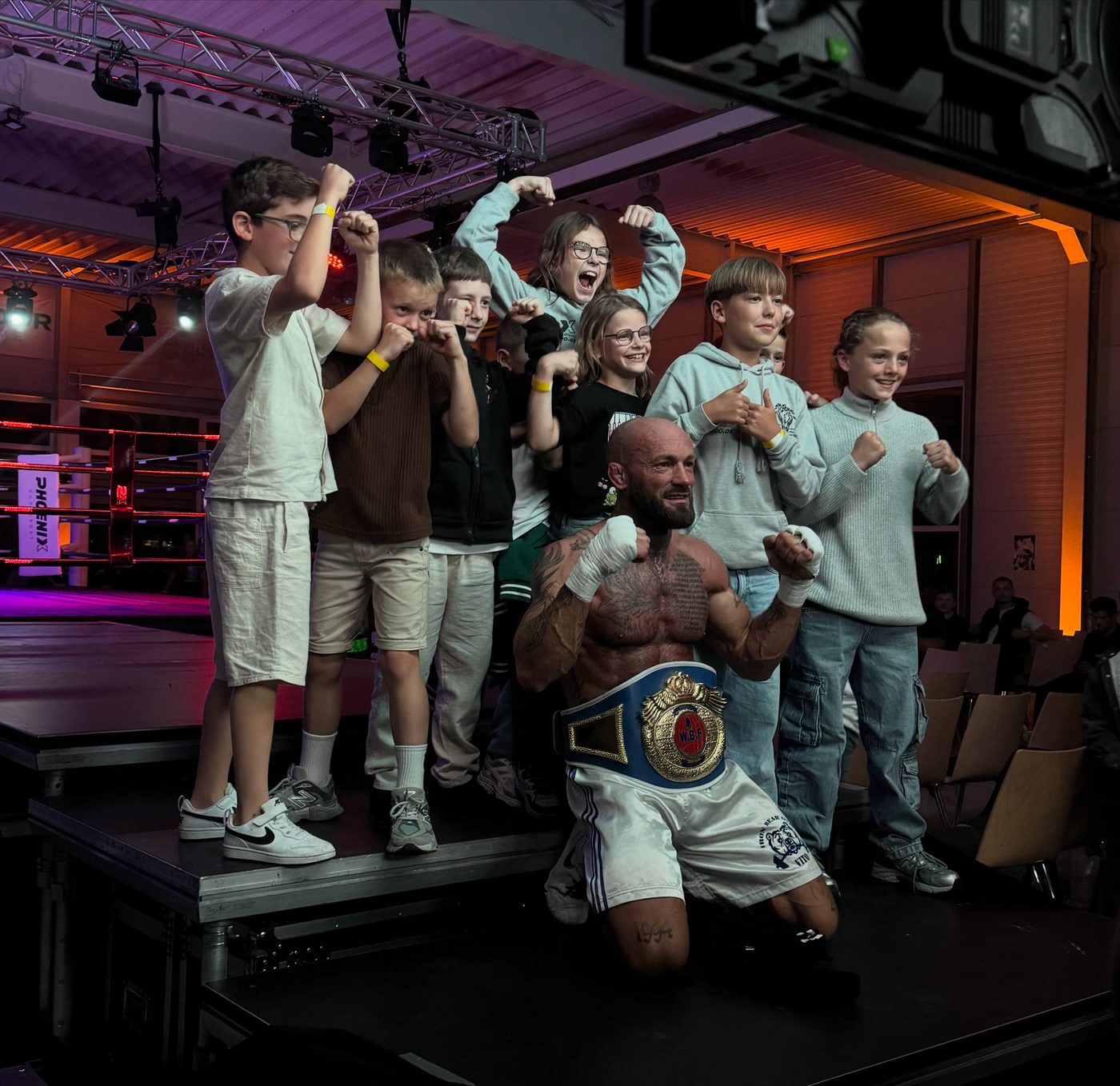 Viktor Kessler mit Meistergürtel, umringt von jubelnden Kindern aus seinem Gym